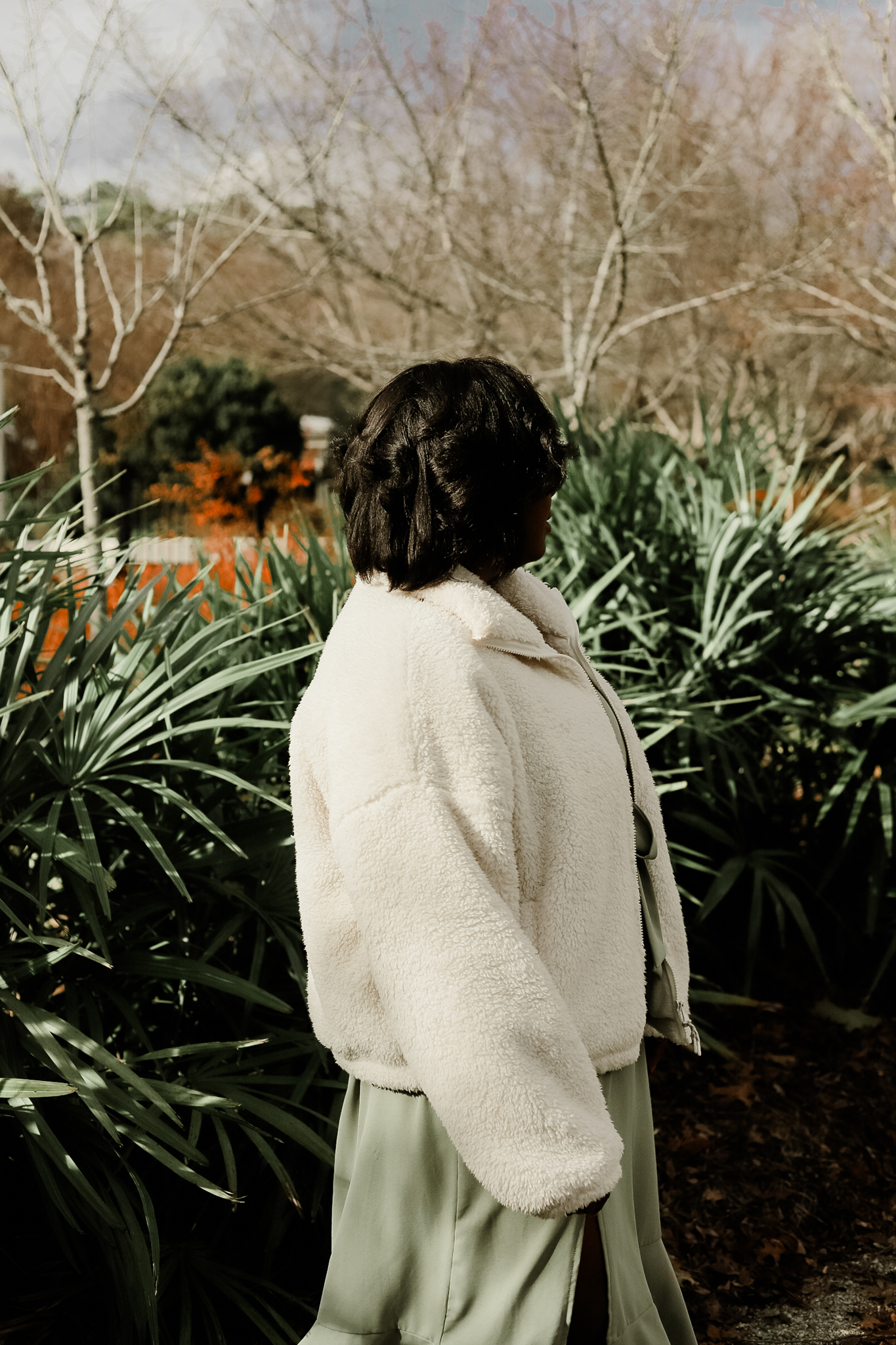 girl in white coat with green dress outside near green leaves